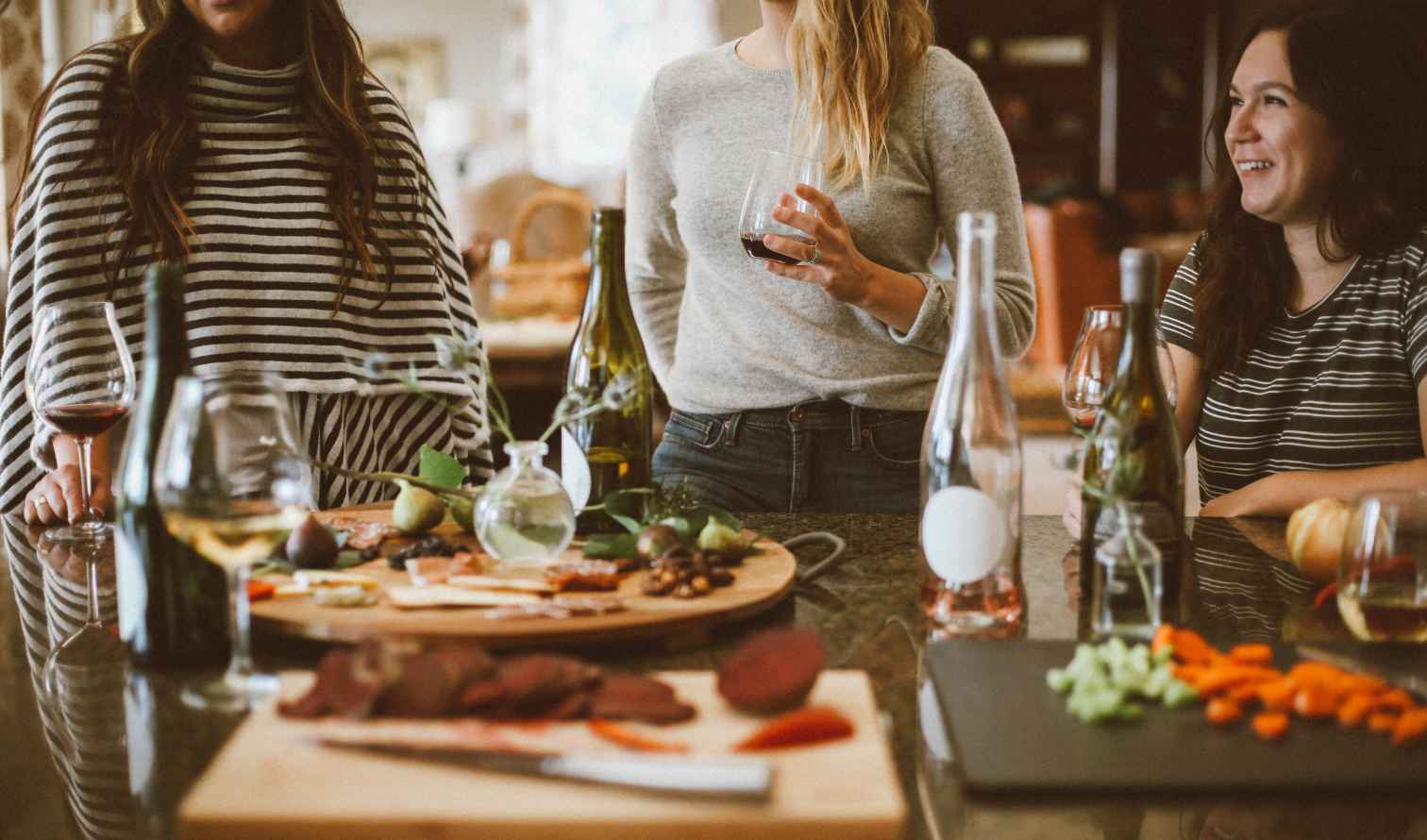 Three people standing around a kitchen island with wine and appetizers in Rome