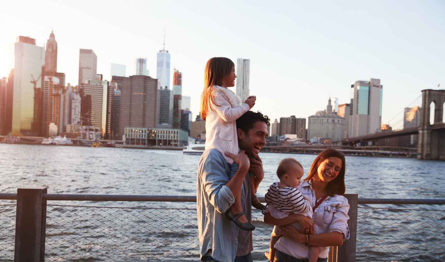 Family on a waterfront promenade with the Brooklyn Bridge in view.