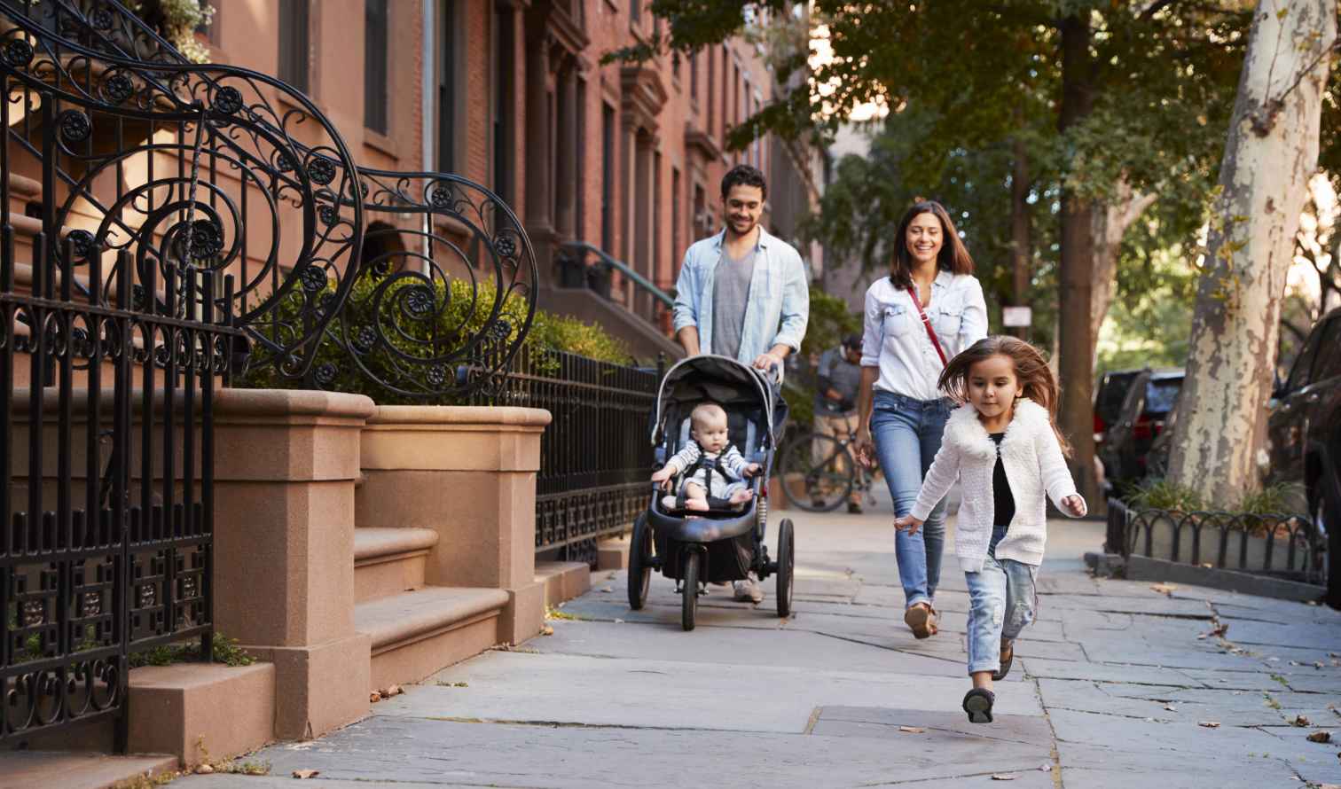 Family walking on a tree-lined street with brownstone buildings in New York