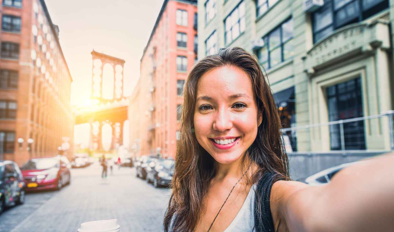 Person taking a selfie on a street in DUMBO, Brooklyn, with Manhattan Bridge visible.