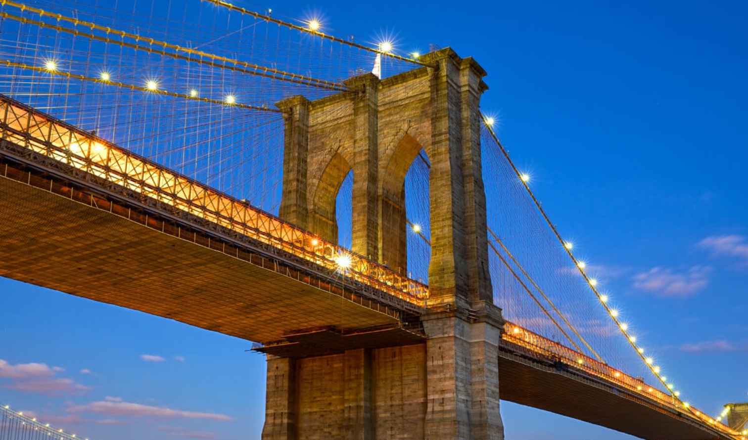 Lights outlining the Brooklyn Bridge and distant Manhattan skyline.