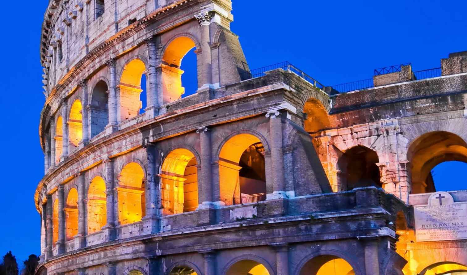 The Colosseum in Rome illuminated against a clear blue sky.
