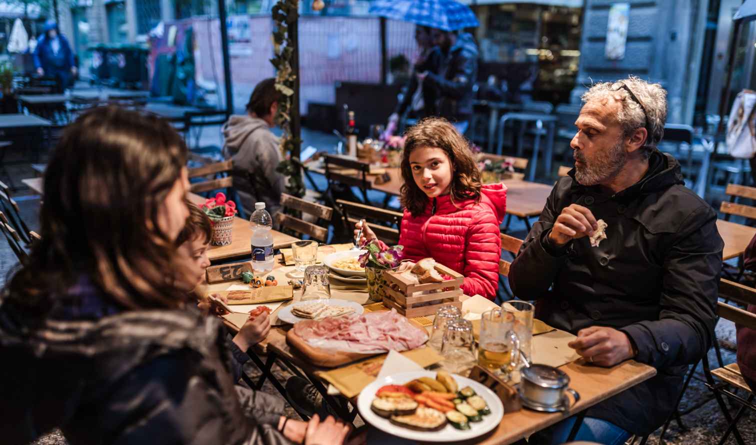 Family enjoying a meal at a wooden table on a street patio in Bologna