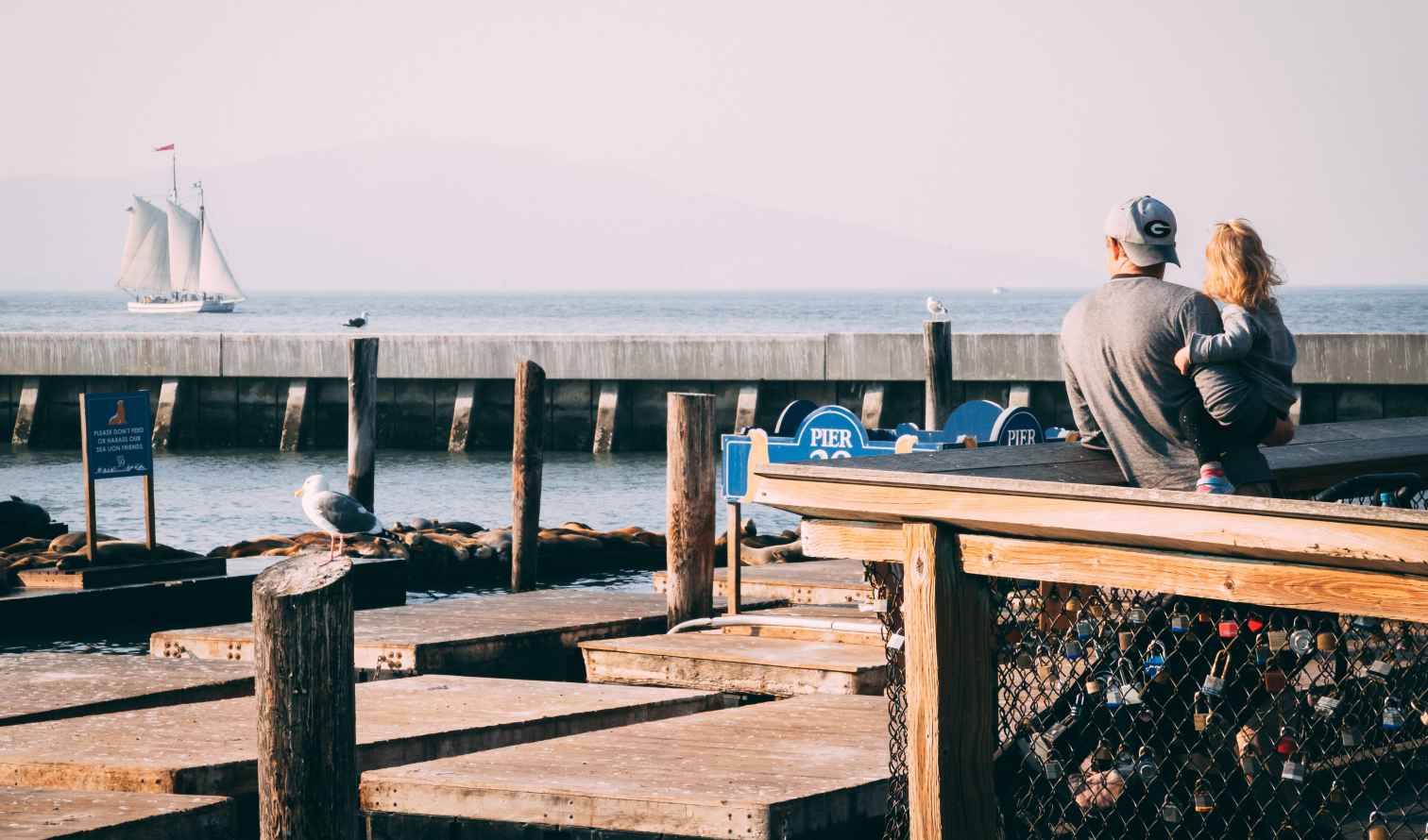 Man holding child at Pier 39 with sailboat in background in San Francisco