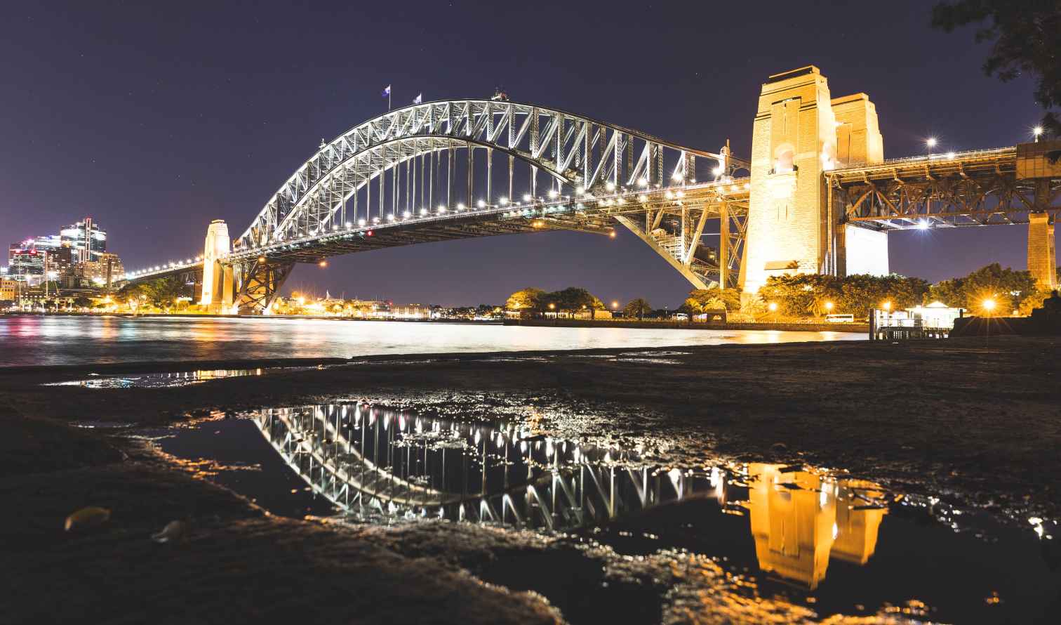 Sydney Harbour Bridge at night with lights reflecting in water.