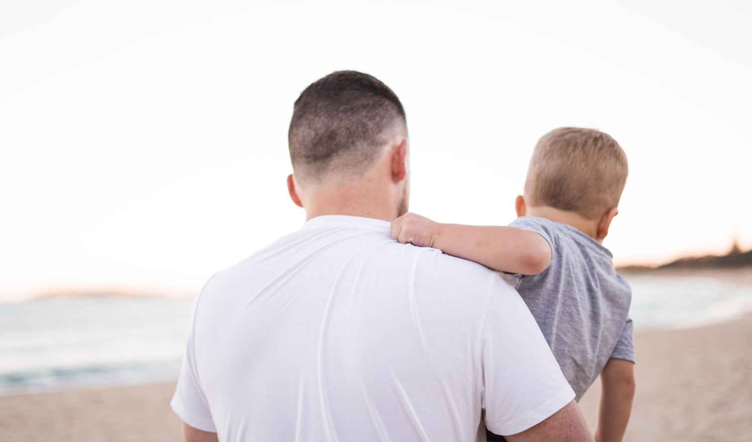 A person carries a child on a beach, white shirt visible in Sydney