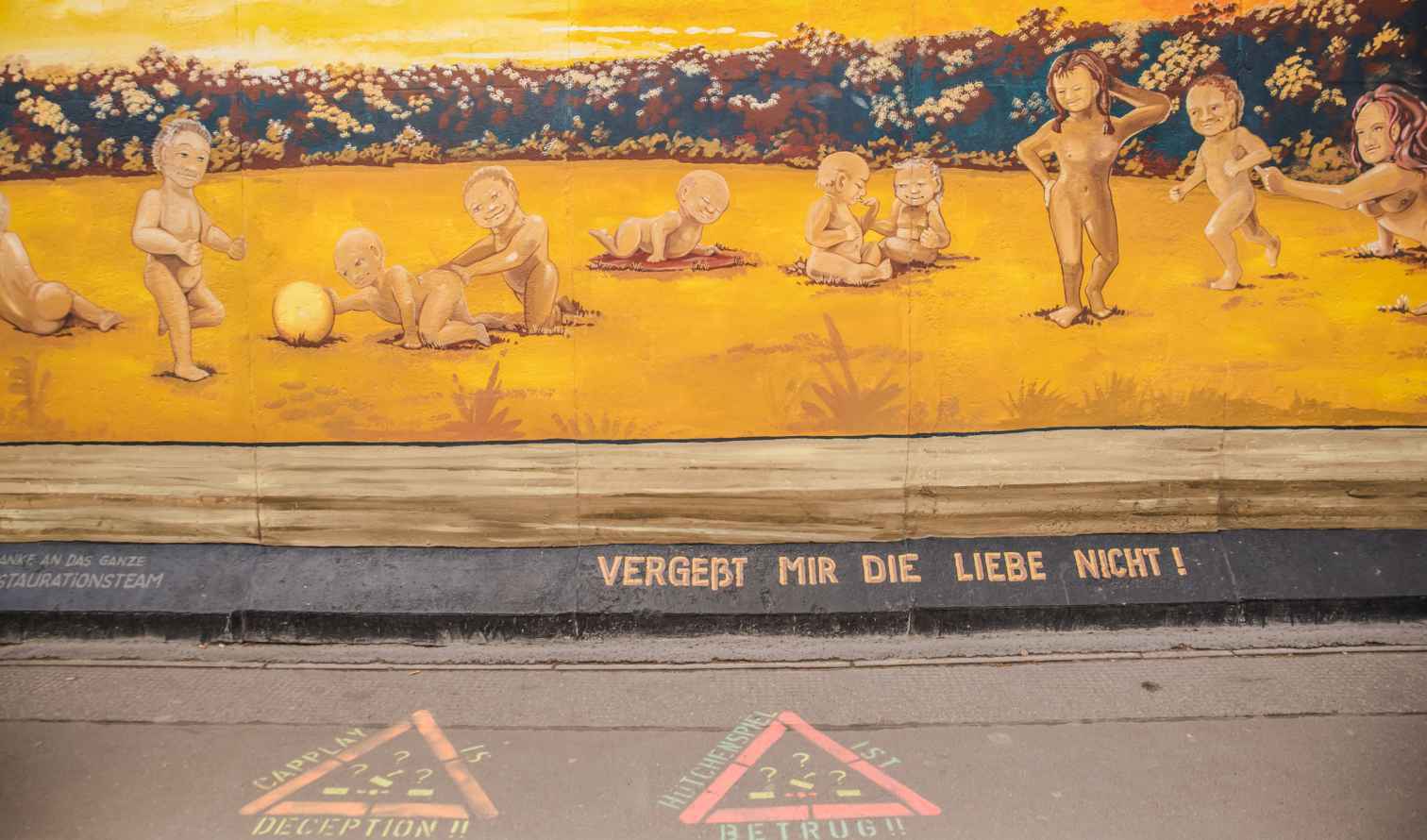 Murals on the Berlin Wall featuring playful cartoon children in a field.