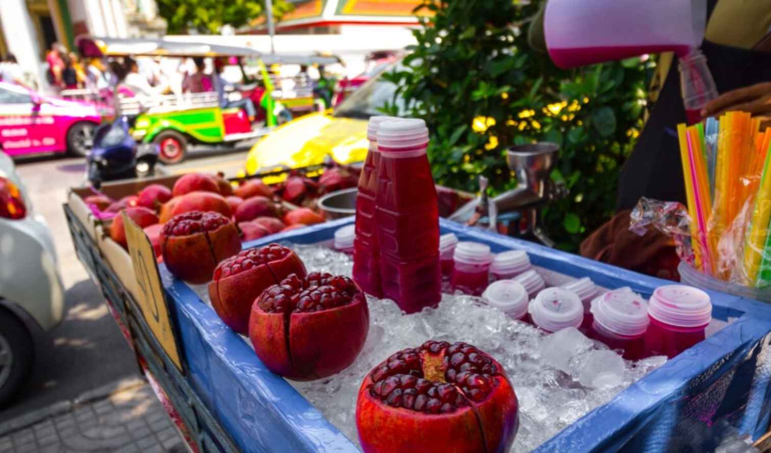 Pomegranate juice stall on a street in Bangkok with tuk-tuks in background.