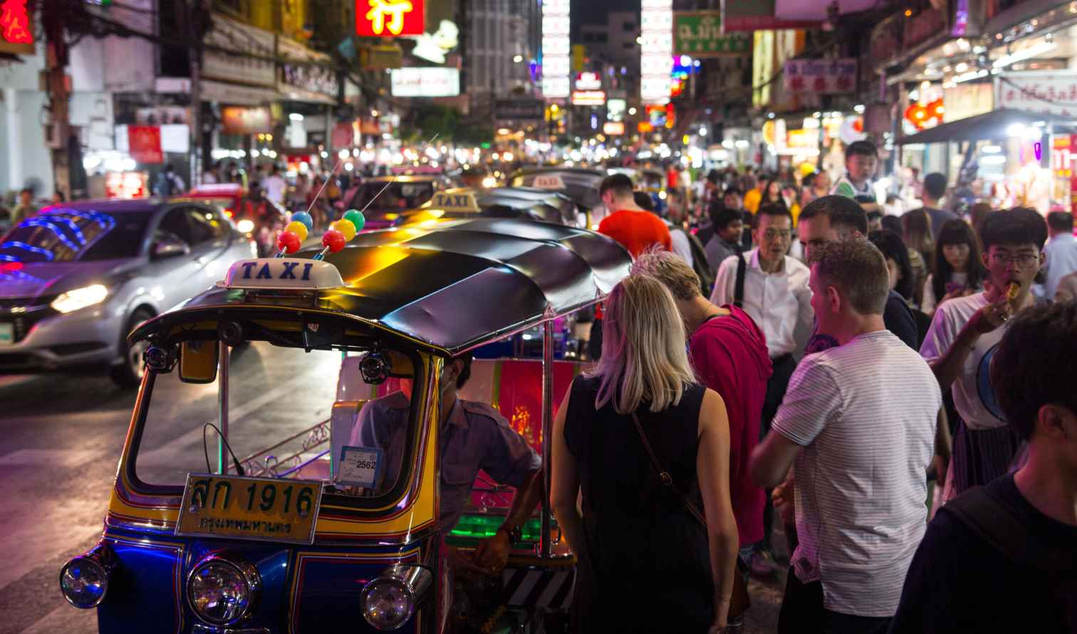 Chinatown in Bangkok with crowds and tuk-tuks on the street.