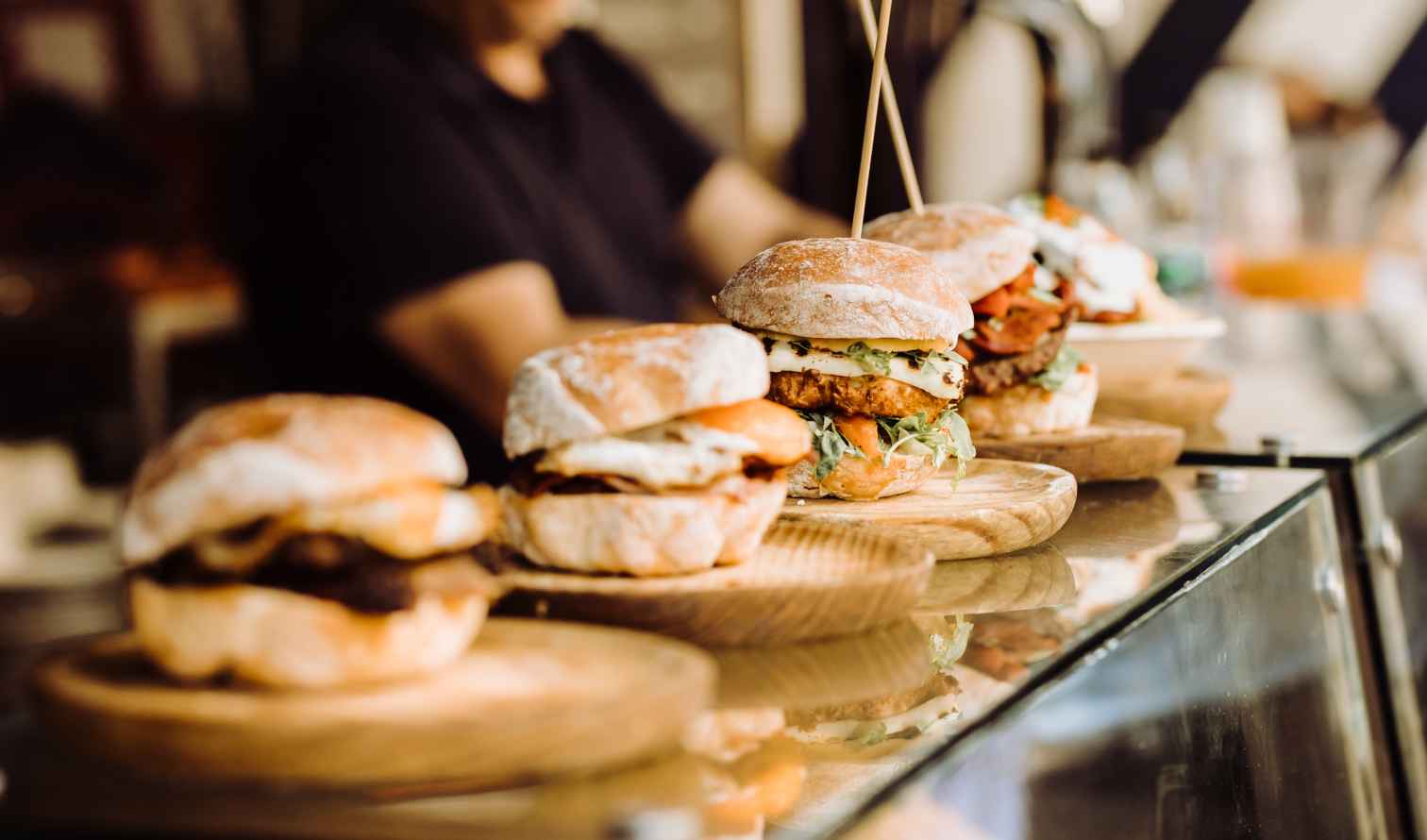 Four burgers on wooden plates with a person in the background in London
