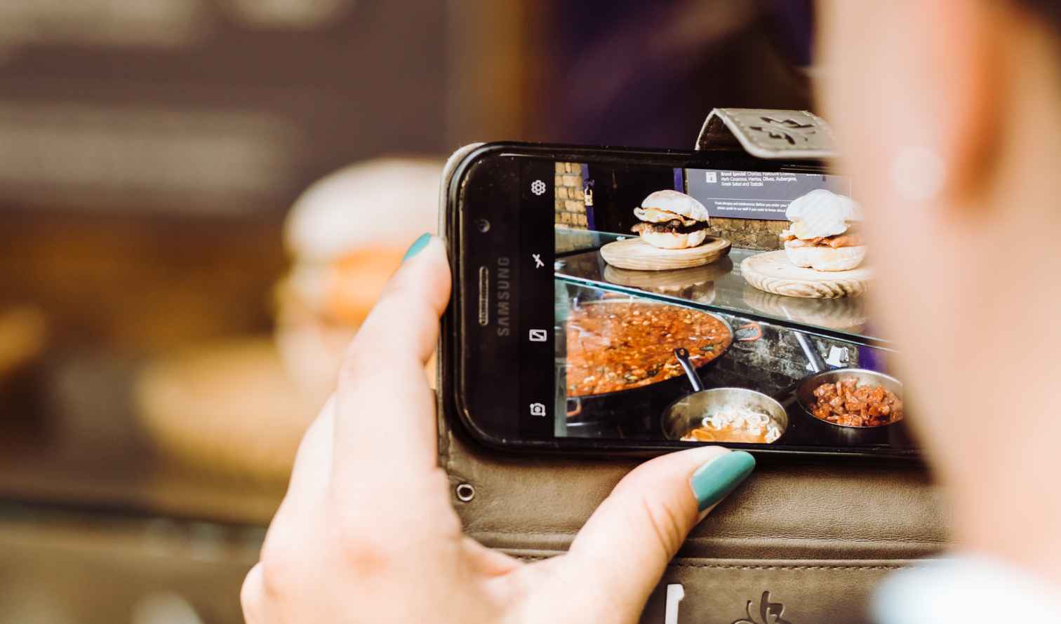 Smartphone capturing an image of burgers and stew at a food stall.
