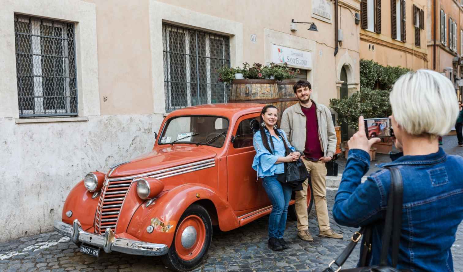 A couple poses by a vintage car on Via della Lungaretta in Rome.