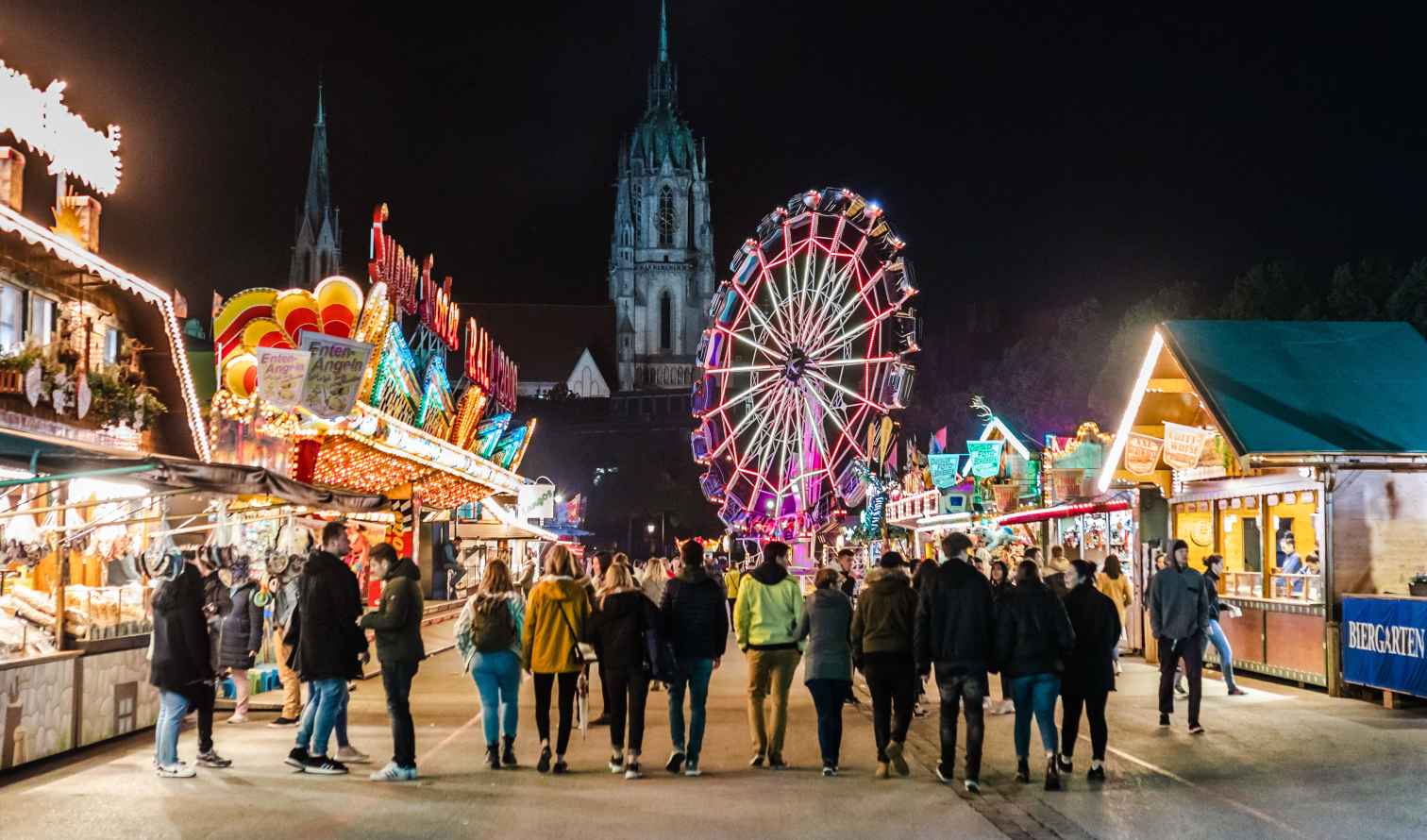 People walking at night at Oktoberfest, Munich, with a Ferris wheel in view.