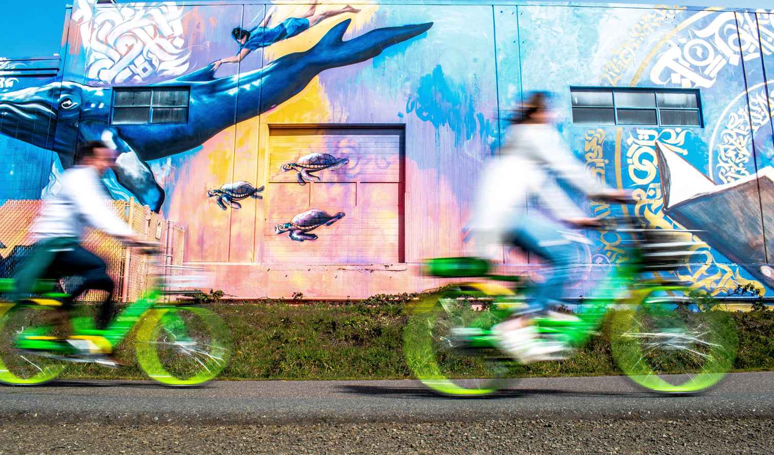 People cycling past a colorful mural with whales and sea creatures in Seattle