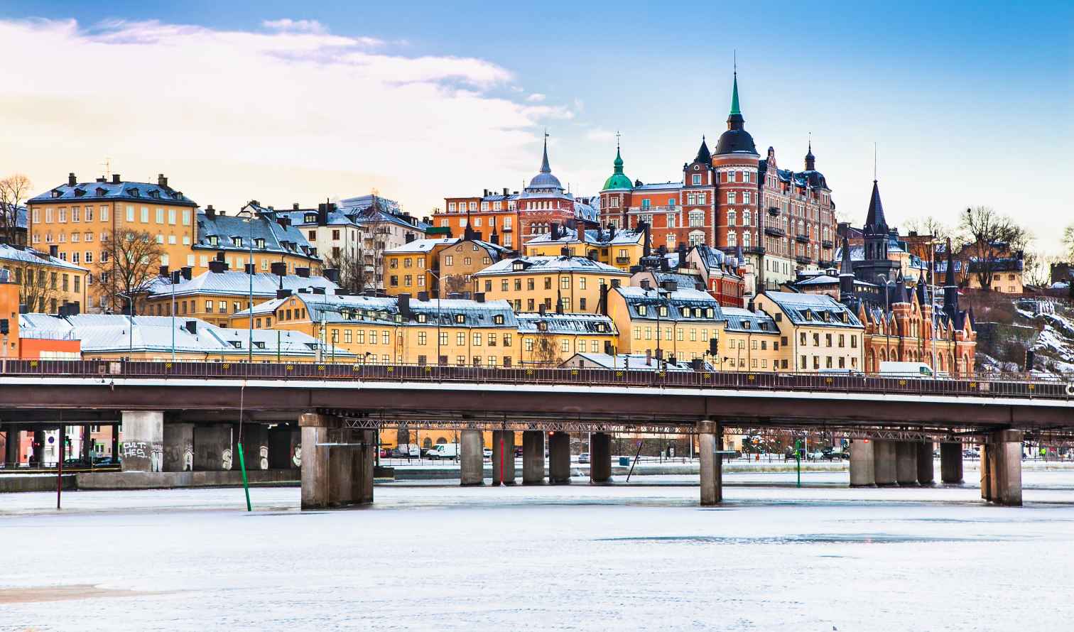 Bridge crossing frozen water with snow-covered buildings in Södermalm, Stockholm.
