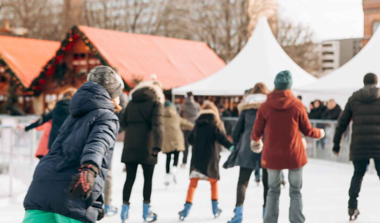 People ice skating on an outdoor rink near Christmas market stalls in Berlin