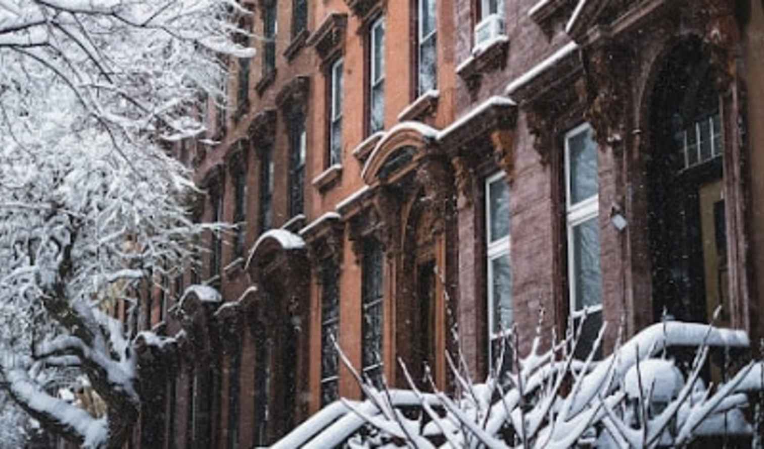 Snow-covered brownstone buildings on a residential street in Brooklyn, New York.