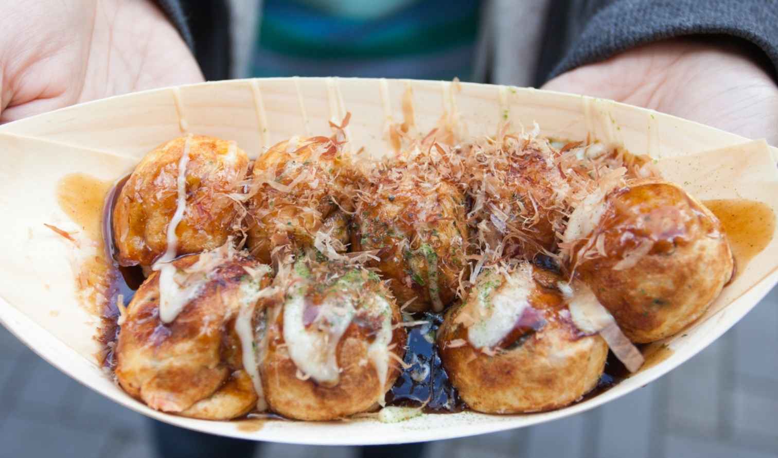 A person holding a tray of takoyaki with bonito flakes in Osaka