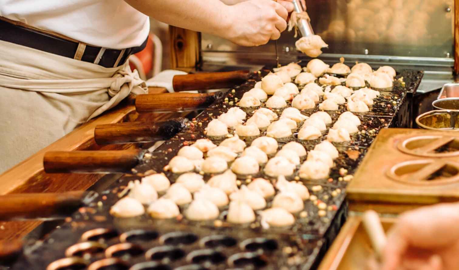 Person preparing takoyaki at a street food stall in Osaka