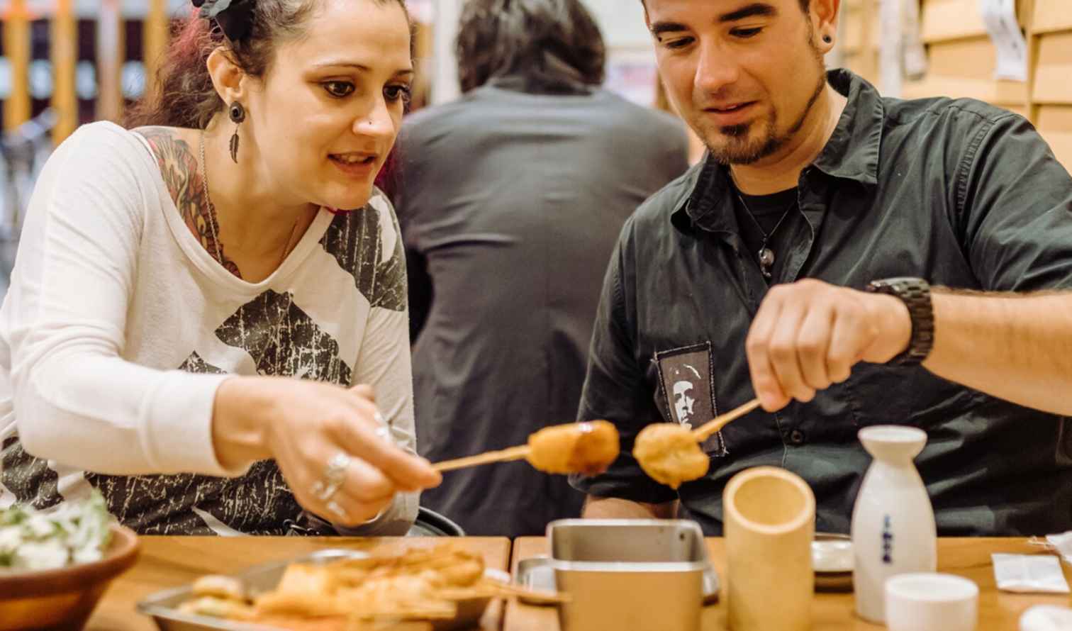 A woman and a man holding food skewers indoors in Osaka