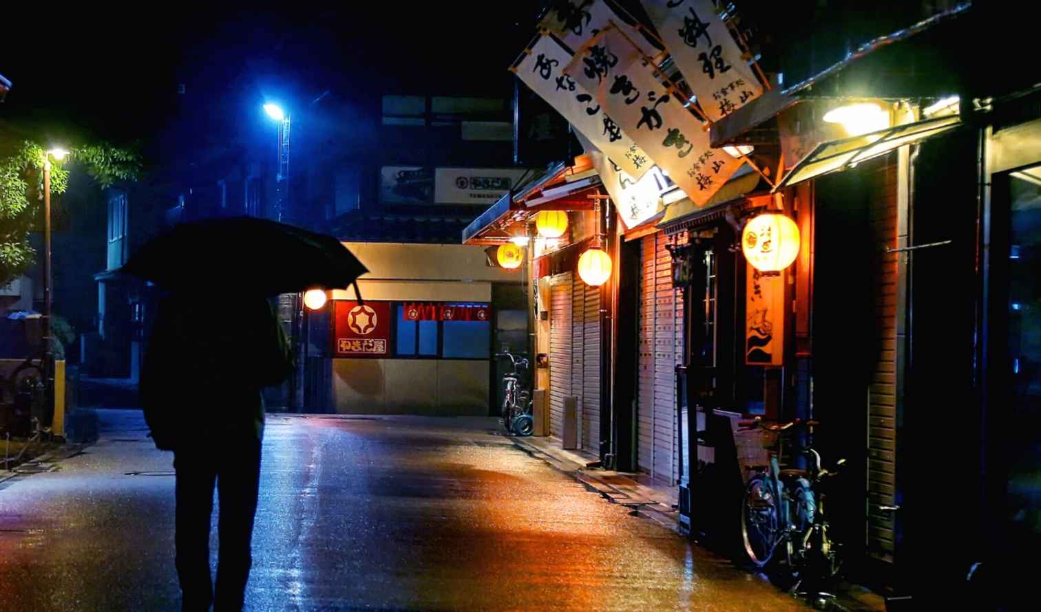 Person with an umbrella on a rainy street in Hiroshima at night.