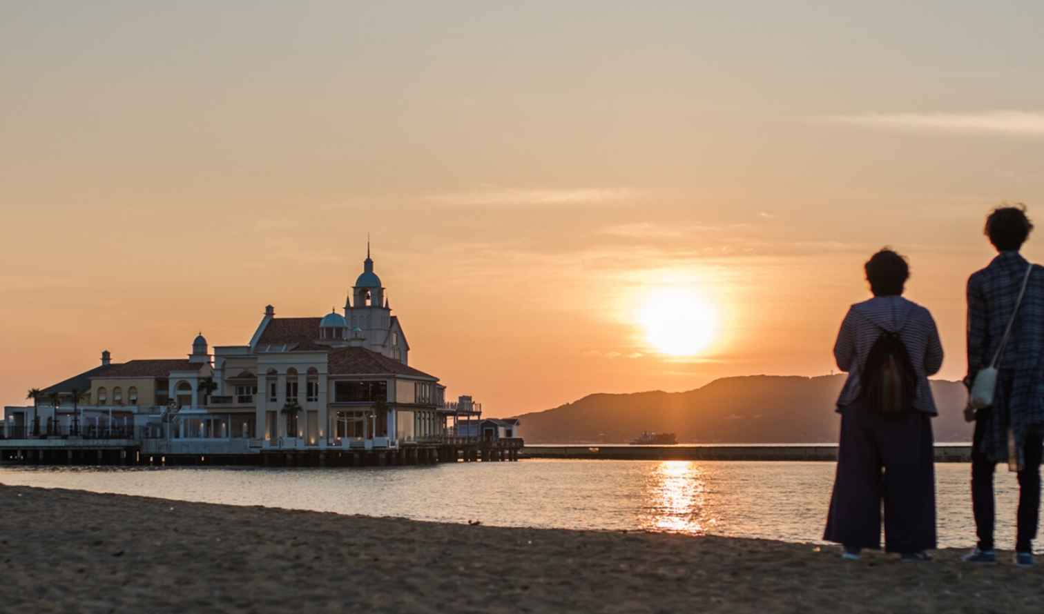 Two people stand on Momochi Beach facing the sunset in Fukuoka, Japan.