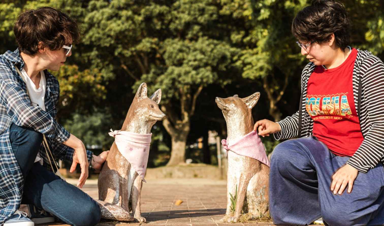 Two people kneeling by kitsune statues in a park setting in Fukuoka