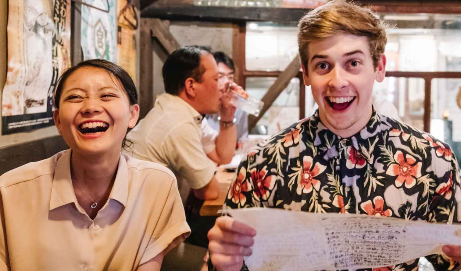 Two people smiling in a Japanese restaurant with posters on the wall in Nagoya