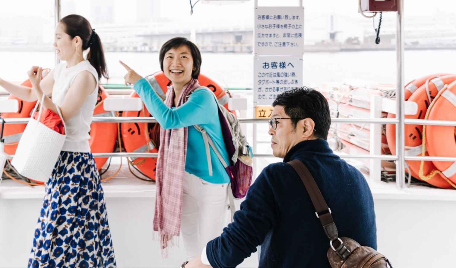 Two women and a man on a ferry, one woman pointing outwards in Yokohama