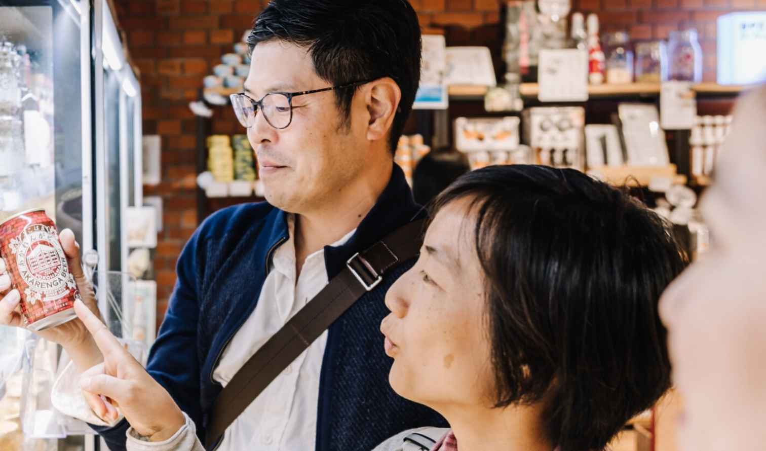 Two people examining a refrigerator of canned drinks in a store in Yokohama