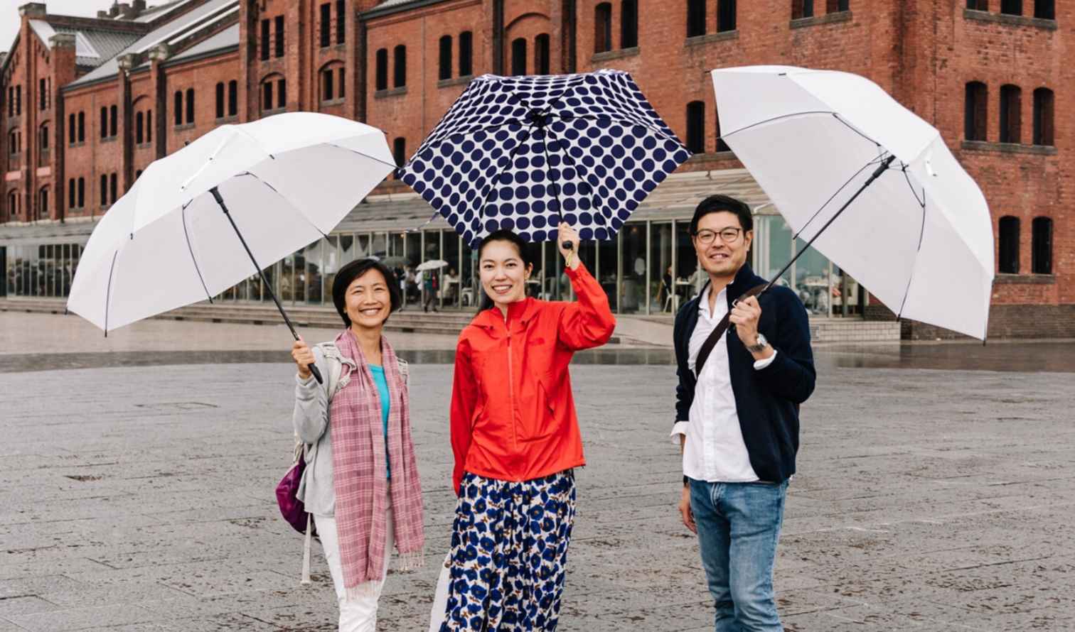 Three people with umbrellas in front of Yokohama Red Brick Warehouse.