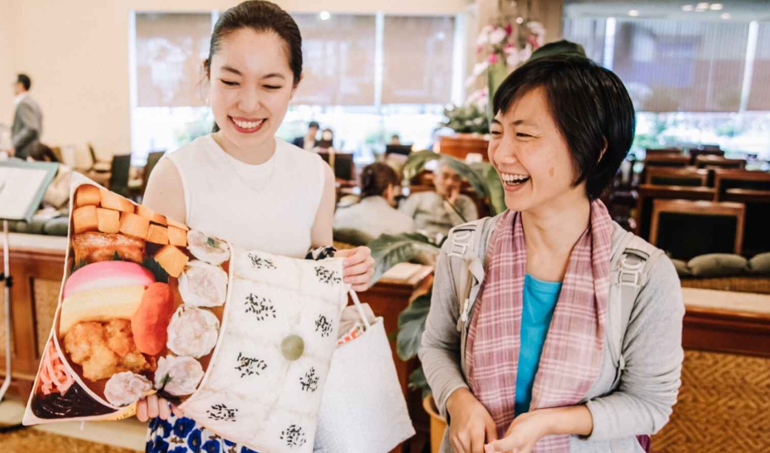 Two women smiling with a unique cushion at a reception area in Yokohama