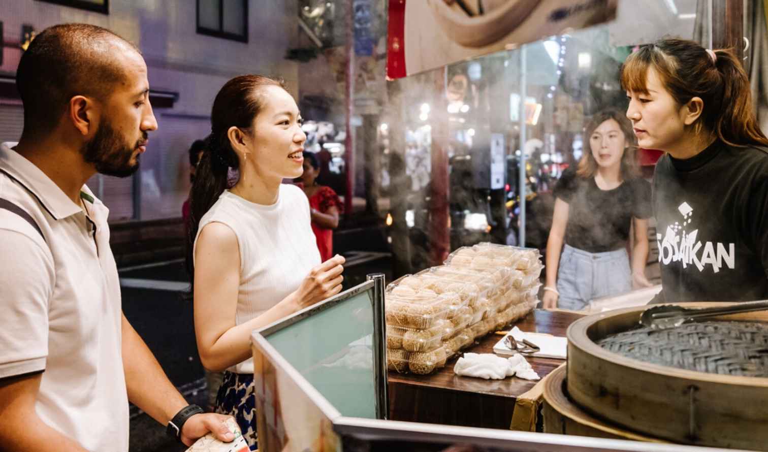 People standing at a street food stall in a city at night in Yokohama