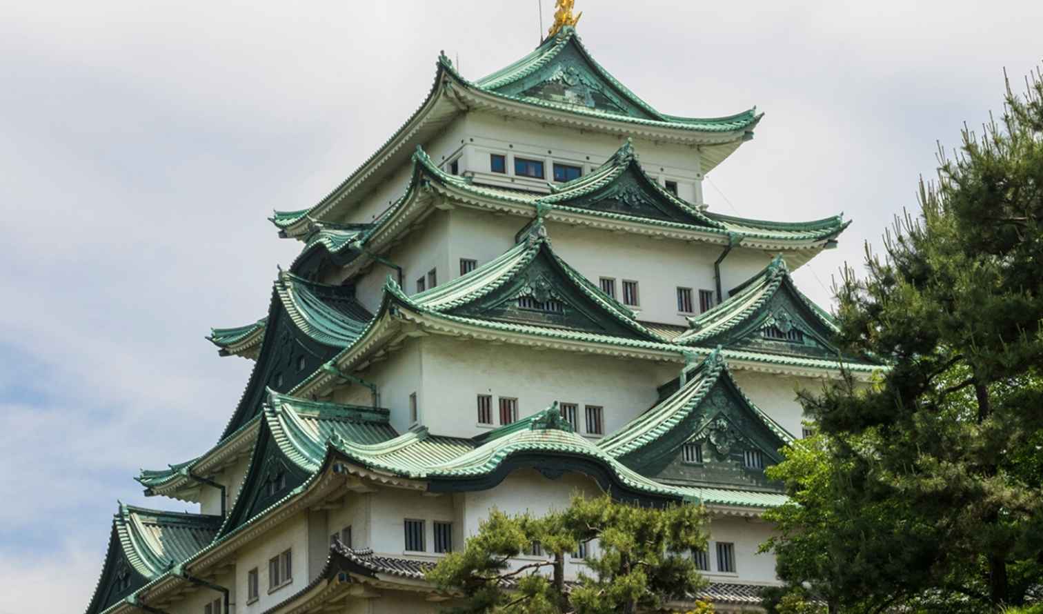 Nagoya Castle with green roof and trees in the foreground.