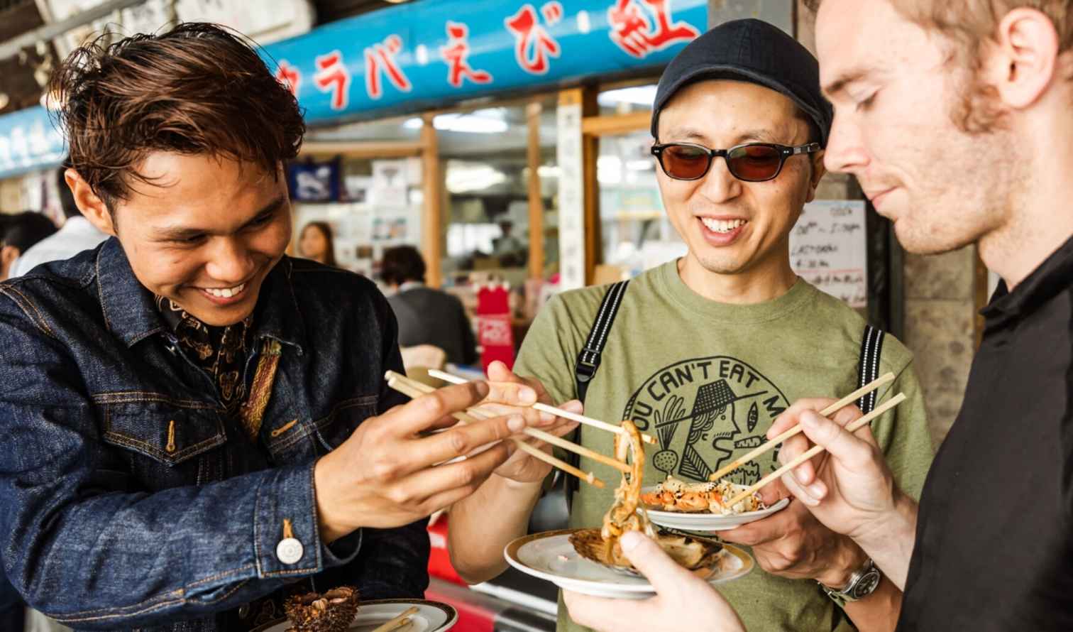 Three men eating food with chopsticks at a street market in Sapporo