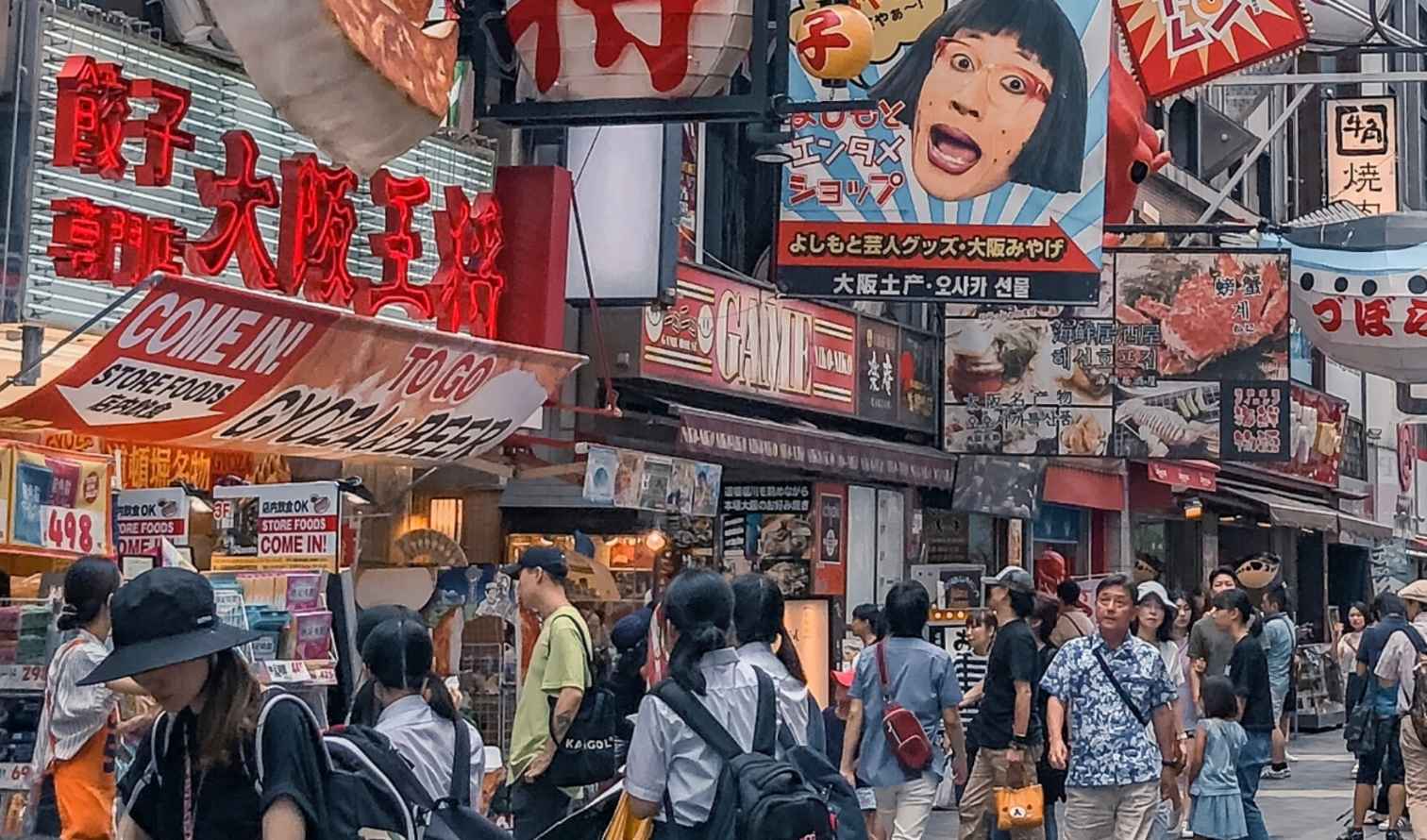 Crowded street in Dotonbori, Osaka with colorful signs and shops.