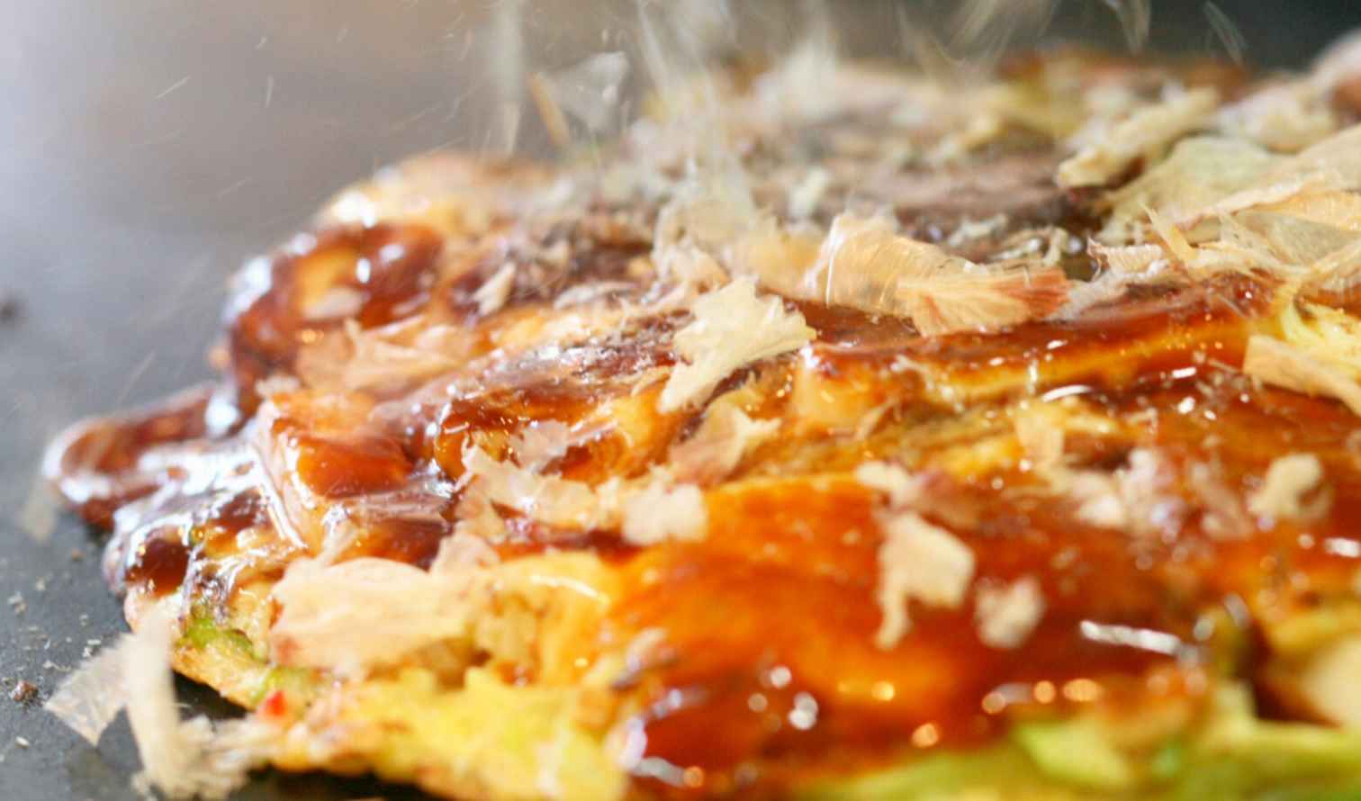 Japanese pancake, okonomiyaki, sizzling with sauce and bonito flakes in Osaka