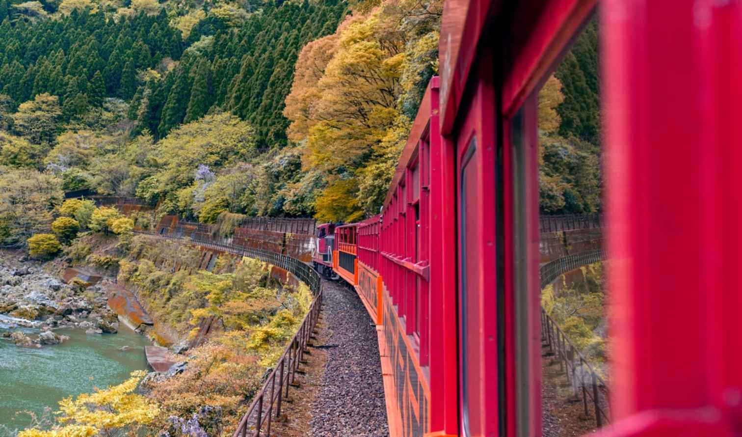 Red train traveling along the Hozugawa River in Kyoto, Japan.