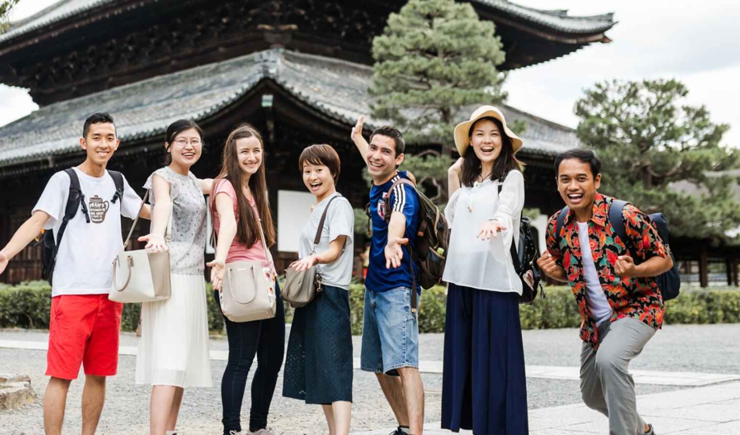 Seven people with backpacks standing near an old wooden structure in Kobe