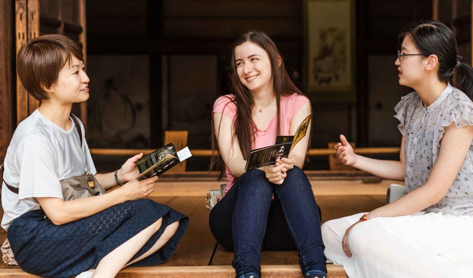 Three women sitting and talking on a wooden porch in Osaka