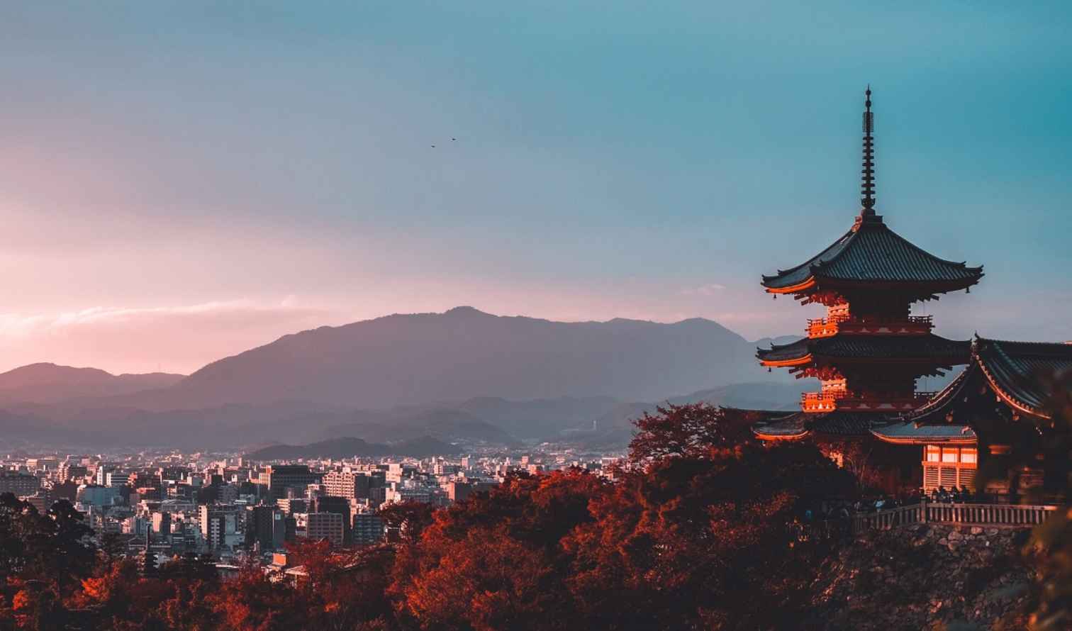 Kiyomizu-dera temple overlooking Kyoto city at sunset with mountains in background.