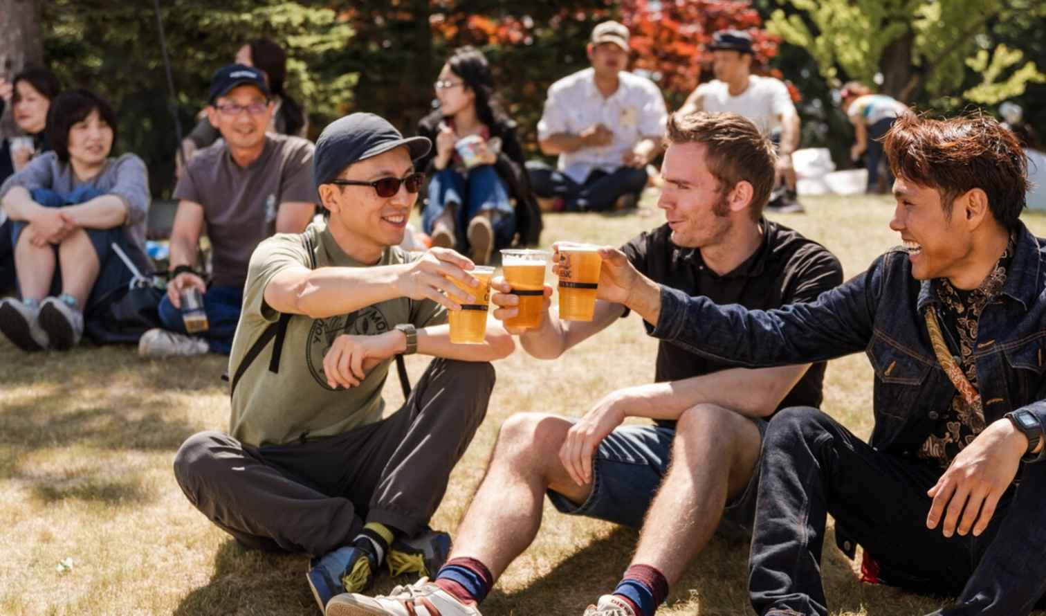People sitting on grass, enjoying drinks in a park setting in Sapporo