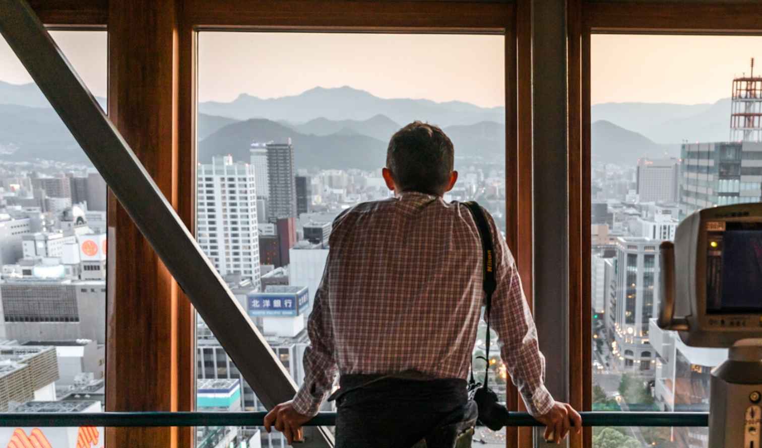 Person looking out from Sapporo Tower's observation deck over cityscape and mountains.