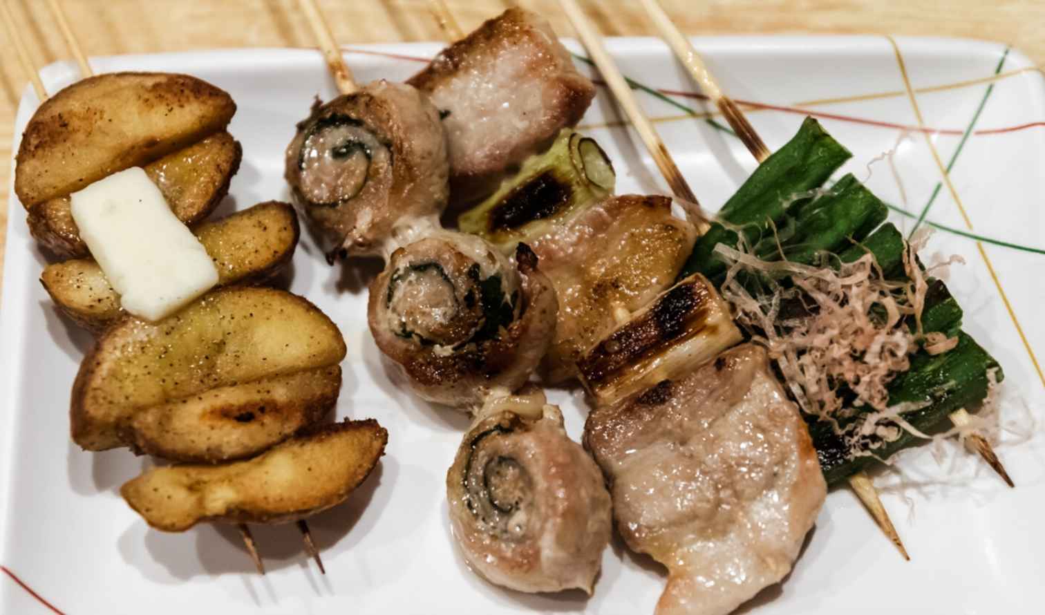Grilled skewers with potatoes and meat on a white plate in Sapporo
