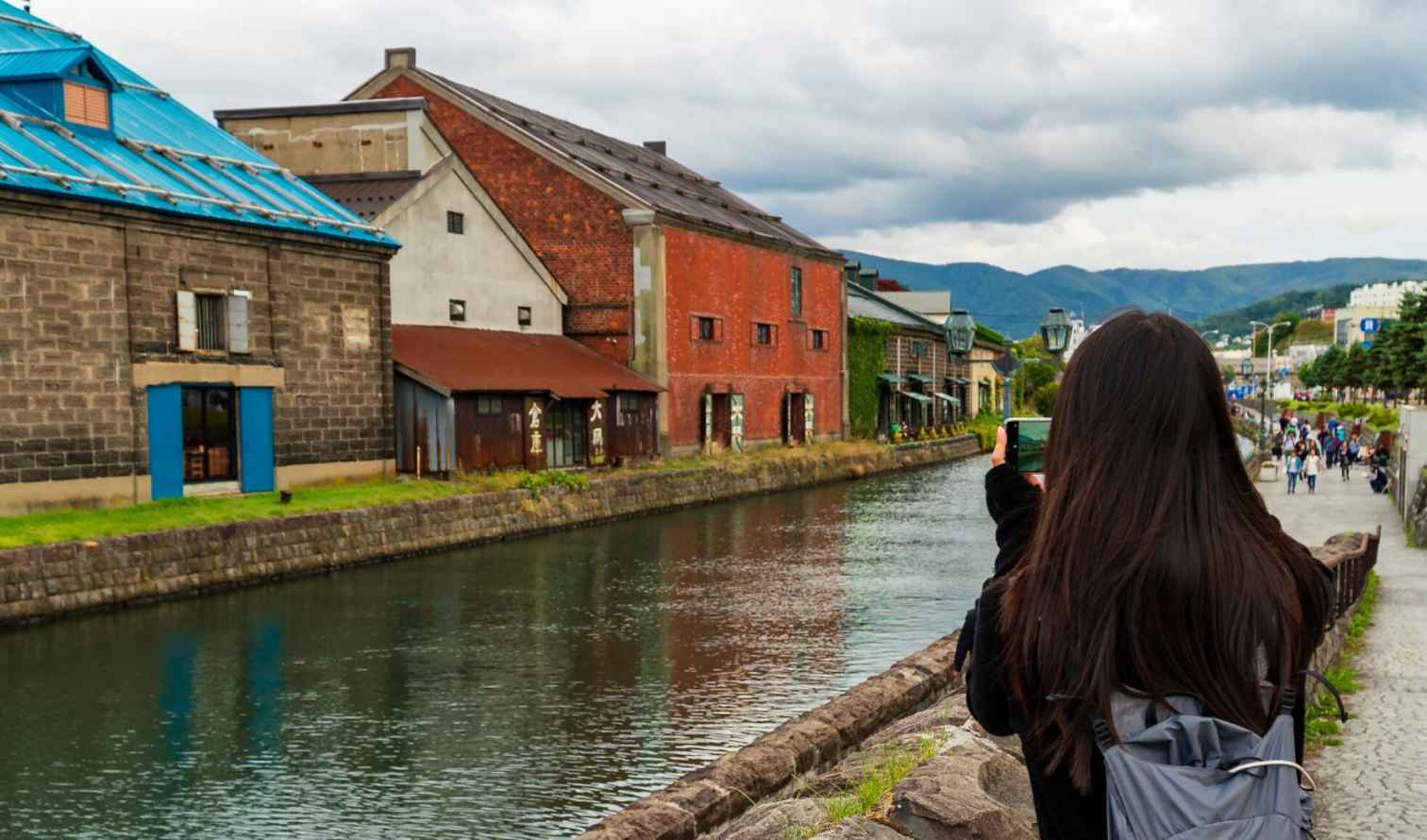 Person taking photo of historic buildings along Otaru Canal, Hokkaido, Japan.