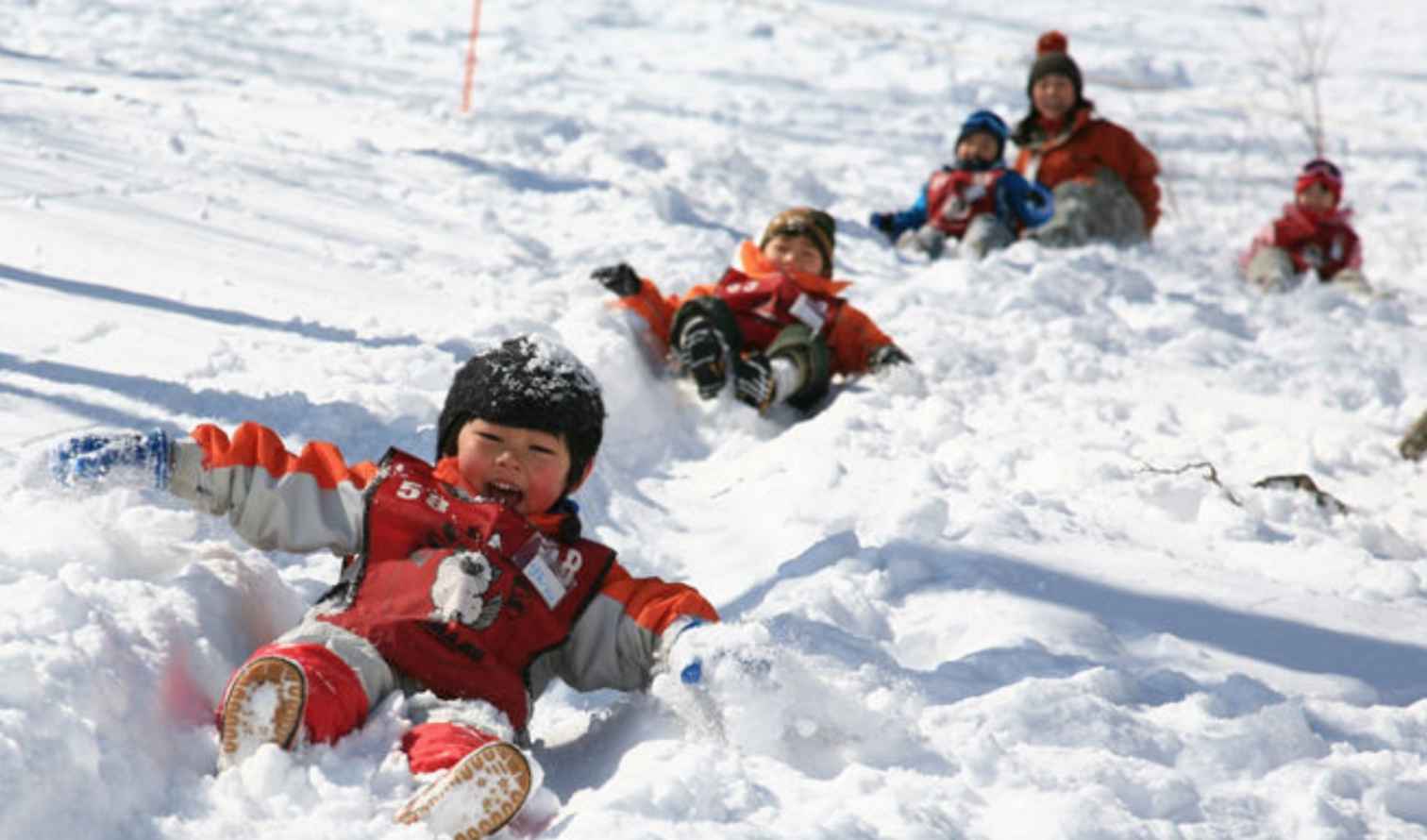 Children in red snowsuits sliding down a snowy hill in Sapporo
