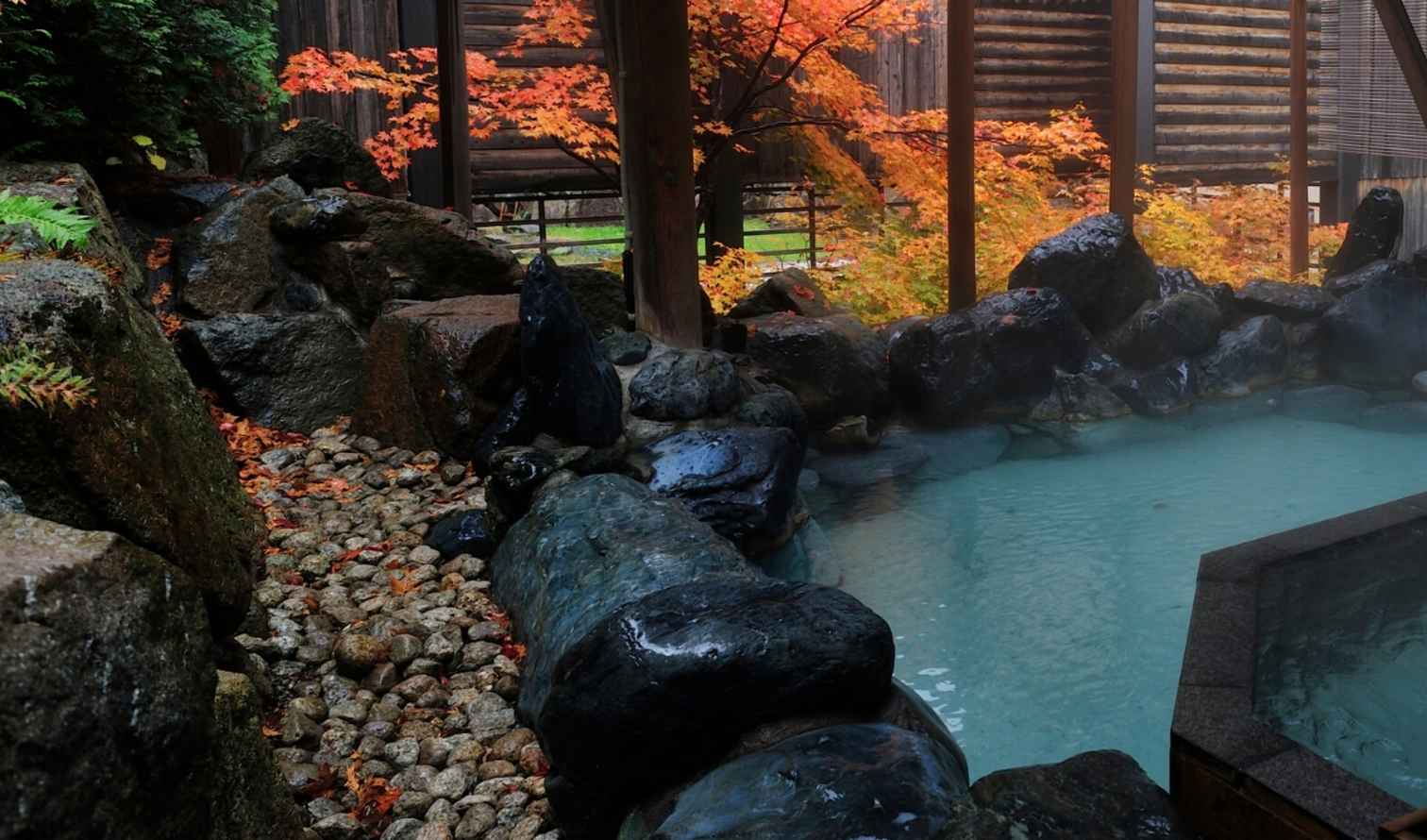 Japanese onsen with stone-lined hot spring pool and wooden structures in Sapporo