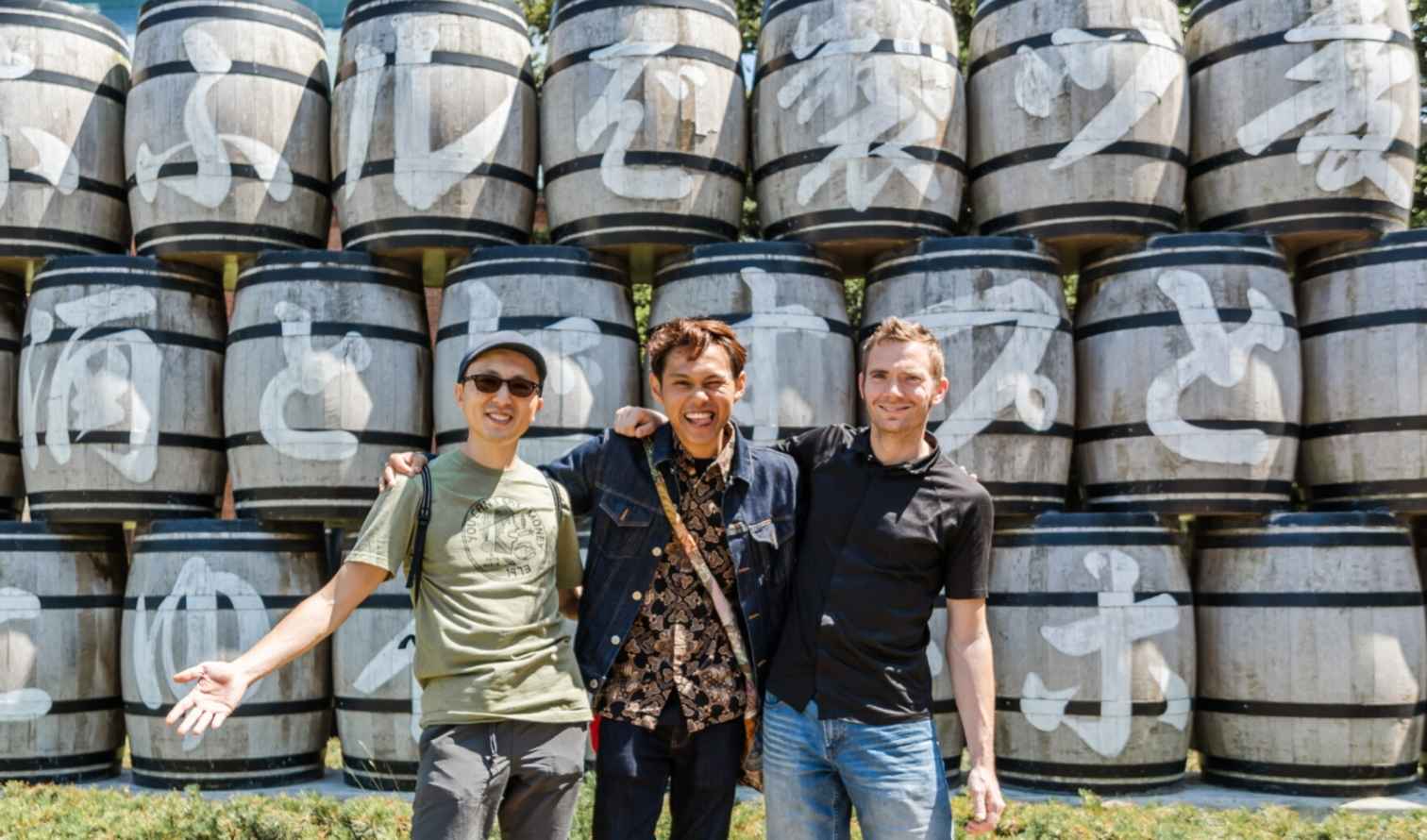 Sake barrels arranged as a backdrop for three visitors at a Japanese site in Sapporo