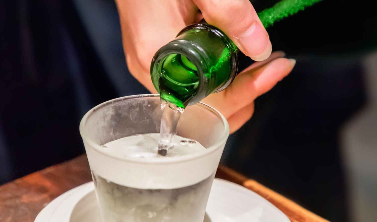 Person pouring liquid into a glass from a green bottle in Sapporo