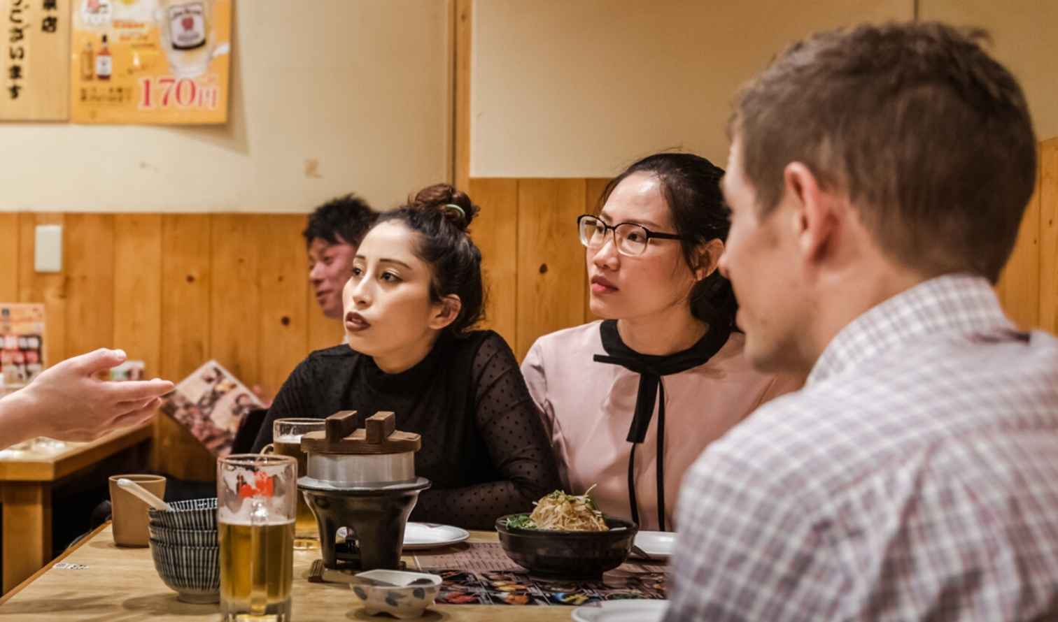 A group of people sitting in a Japanese restaurant talking to a server in Sapporo